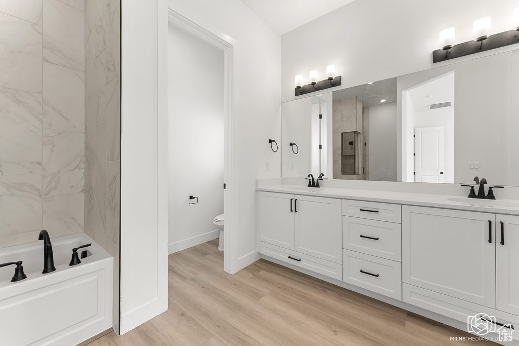 Bathroom featuring toilet, a tub to relax in, hardwood / wood-style flooring, and vanity