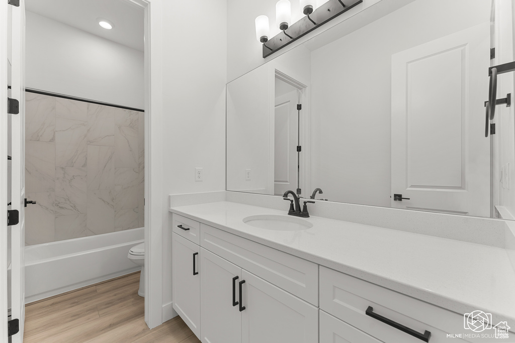 Full bathroom with vanity, toilet, tiled shower / bath combo, and wood-type flooring