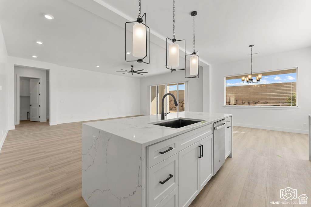 Kitchen with a kitchen island with sink, sink, light stone countertops, white cabinets, and light hardwood / wood-style floors