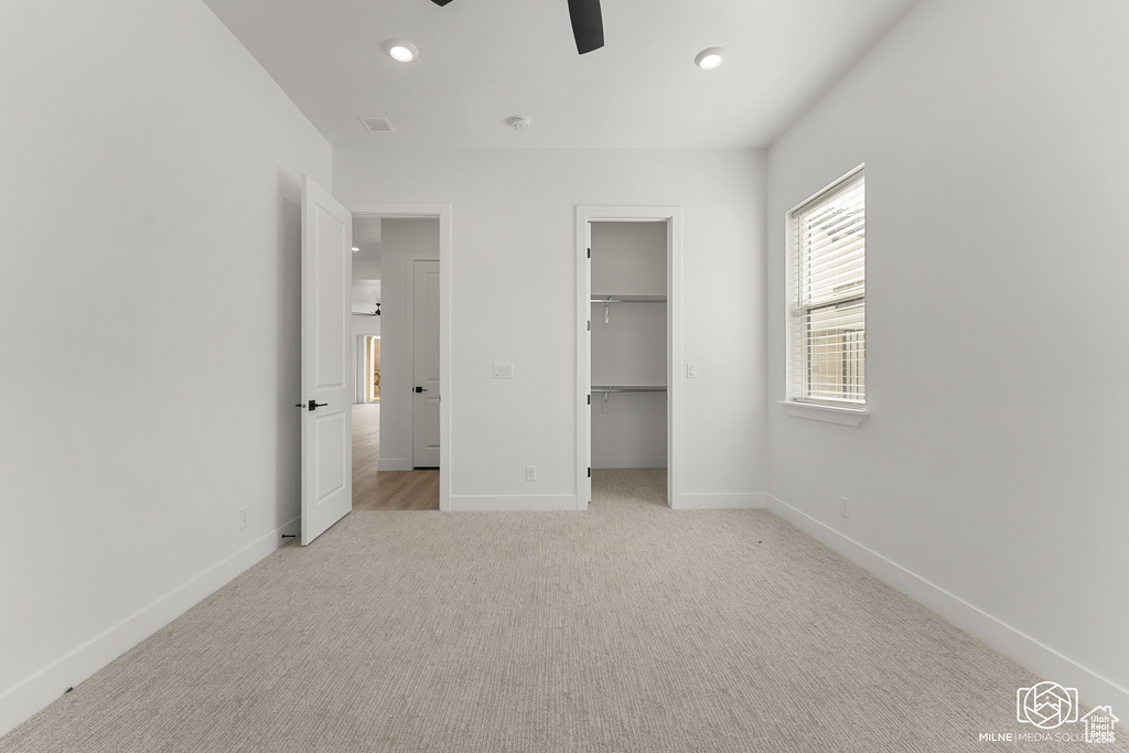 Unfurnished bedroom featuring light carpet, a walk in closet, a closet, and ceiling fan