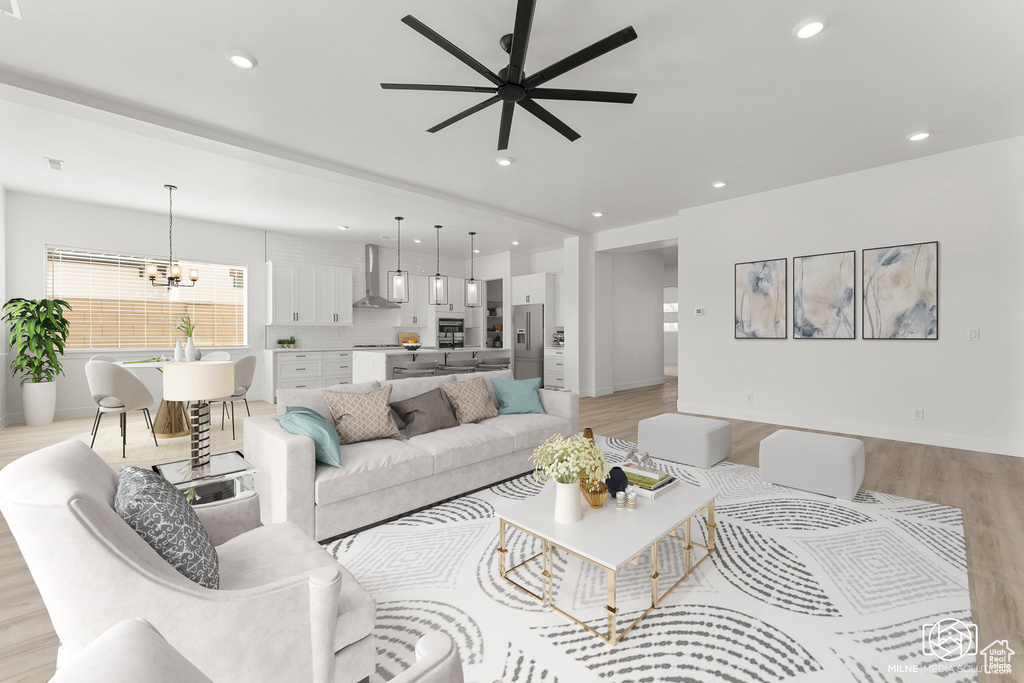 Living room with ceiling fan with notable chandelier and light wood-type flooring