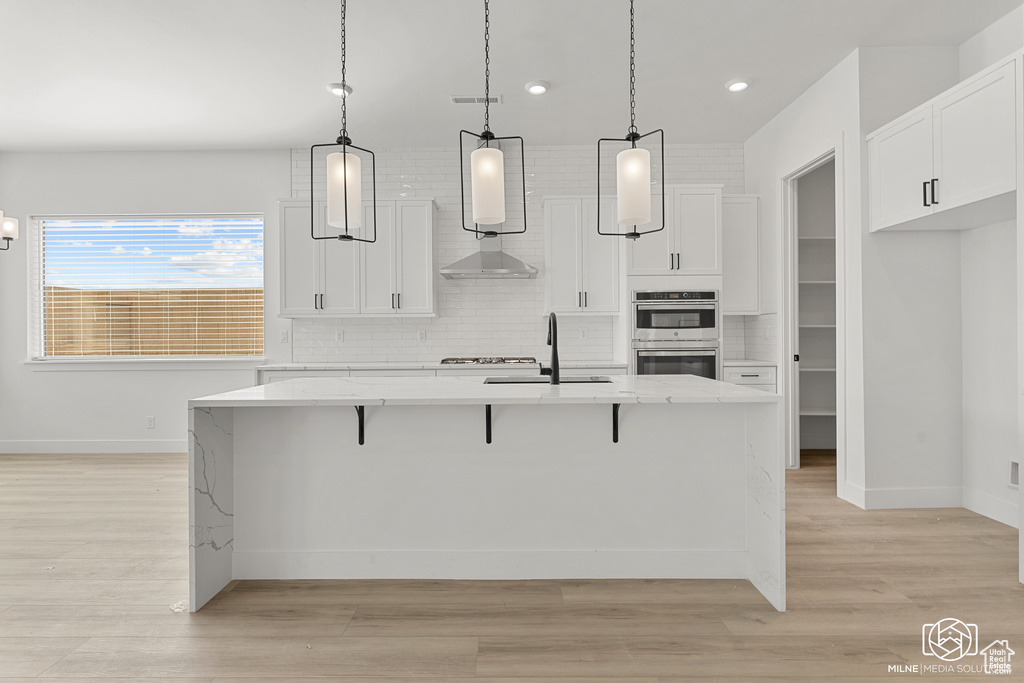 Kitchen featuring pendant lighting, white cabinetry, and an island with sink