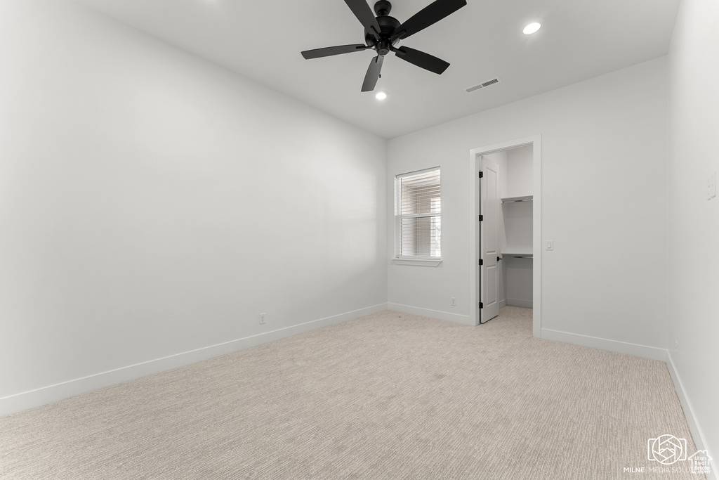 Unfurnished bedroom featuring a closet, ceiling fan, light carpet, and a walk in closet