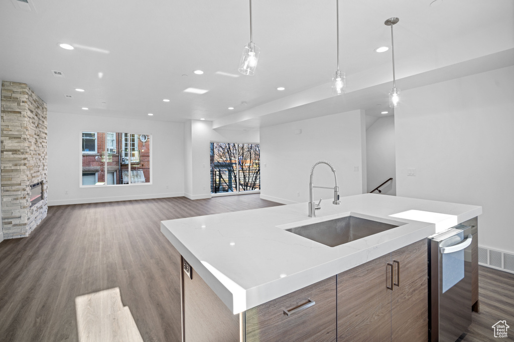 Kitchen featuring pendant lighting, dark hardwood / wood-style floors, a kitchen island with sink, sink, and a stone fireplace