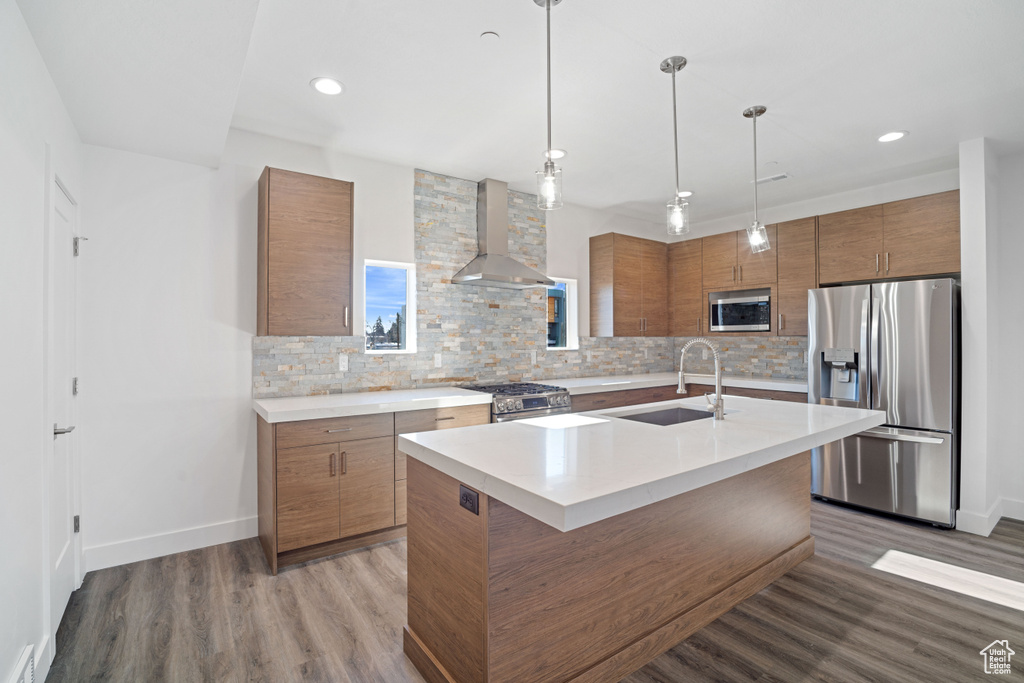 Kitchen with pendant lighting, sink, wood-type flooring, wall chimney exhaust hood, and appliances with stainless steel finishes