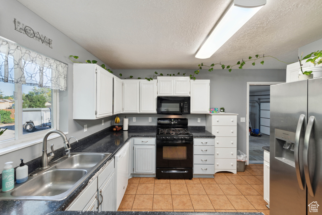 Kitchen featuring a textured ceiling, light tile patterned flooring, sink, white cabinets, and black appliances