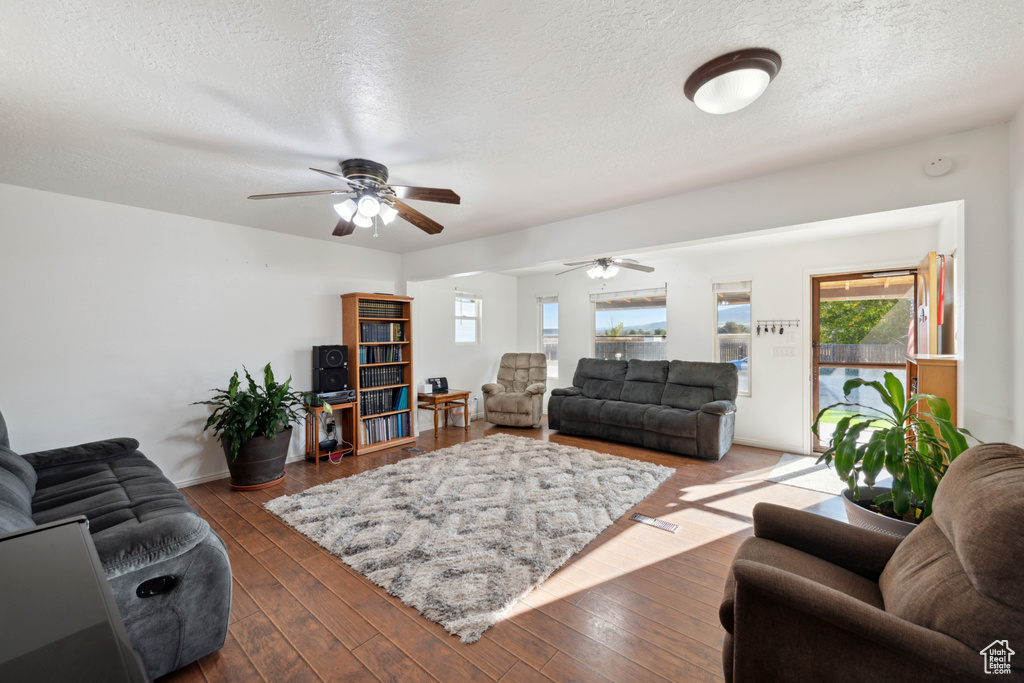 Living room with ceiling fan, a textured ceiling, and dark wood-type flooring