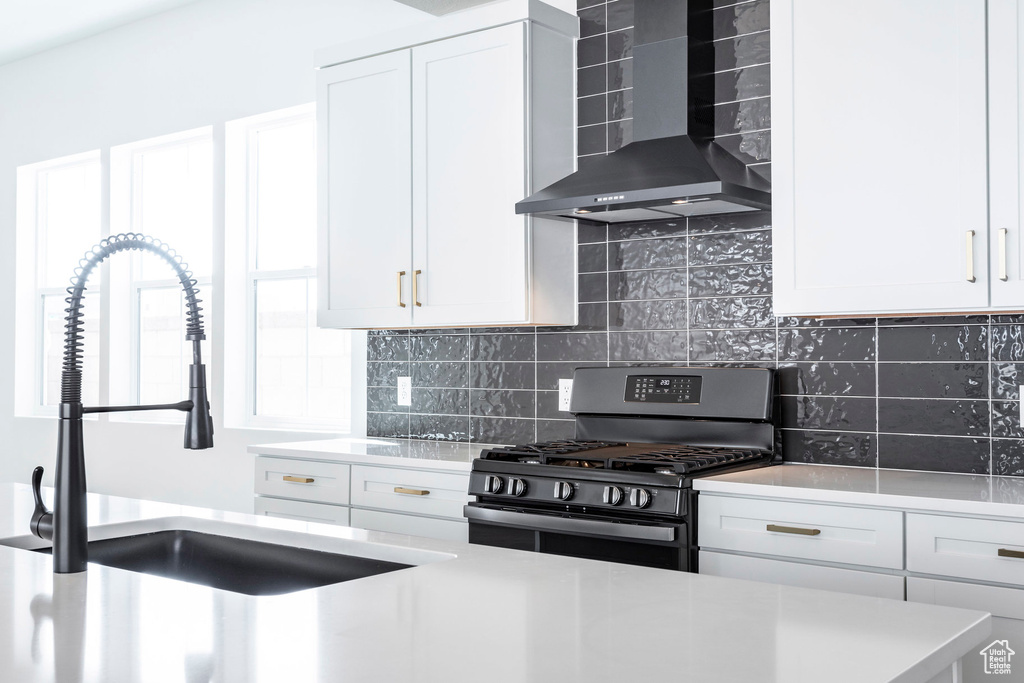 Kitchen featuring sink, range with gas stovetop, wall chimney range hood, white cabinetry, and decorative backsplash