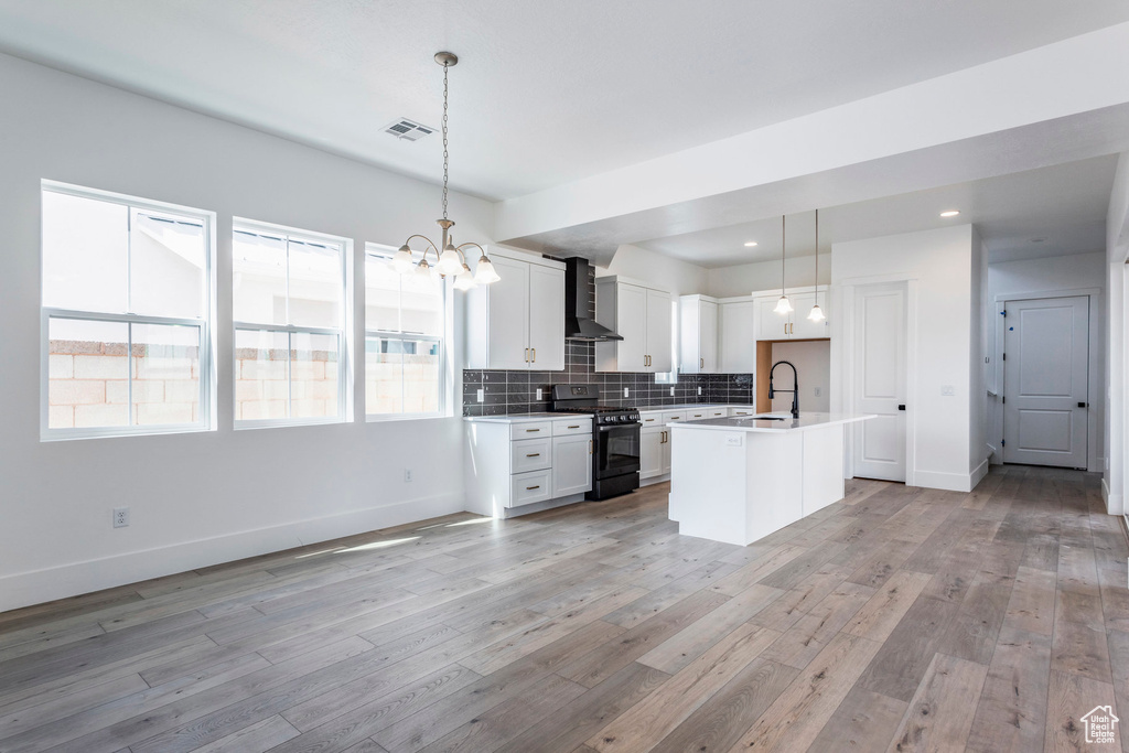 Kitchen featuring hanging light fixtures, white cabinetry, black gas range oven, light hardwood / wood-style flooring, and a kitchen island with sink