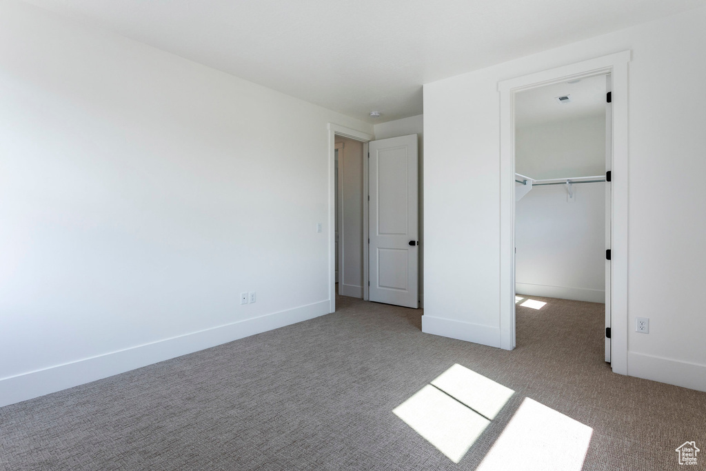 Unfurnished bedroom featuring light carpet, a walk in closet, and a closet