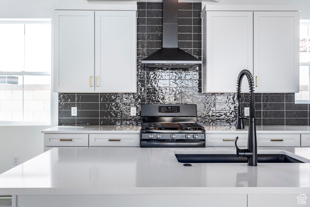 Kitchen featuring stainless steel range with gas cooktop, wall chimney exhaust hood, white cabinetry, and tasteful backsplash