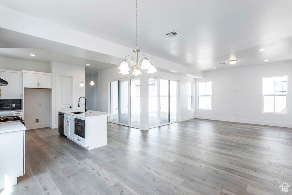 Kitchen featuring white cabinets, pendant lighting, sink, a kitchen island with sink, and light wood-type flooring