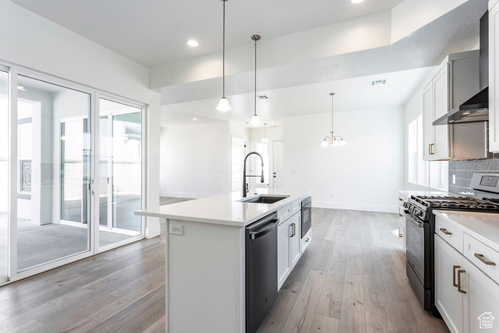 Kitchen featuring appliances with stainless steel finishes, hanging light fixtures, white cabinetry, an island with sink, and backsplash