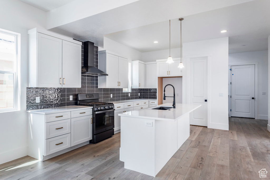 Kitchen with a kitchen island with sink, sink, white cabinets, wall chimney range hood, and black range with gas stovetop