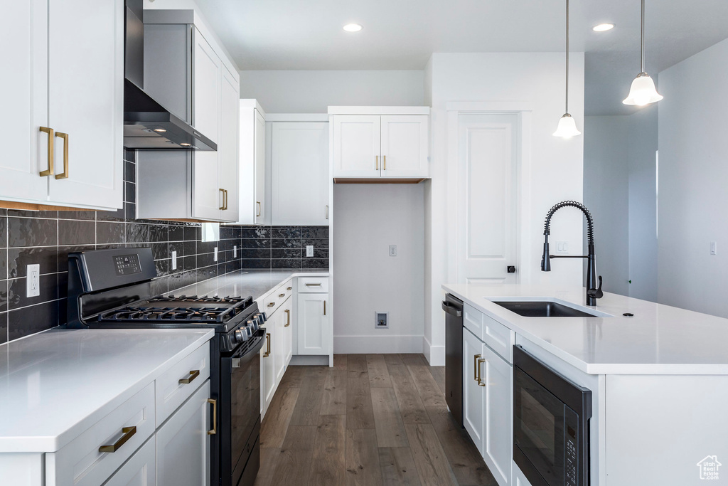 Kitchen with white cabinets, stainless steel appliances, decorative light fixtures, a center island with sink, and wall chimney range hood