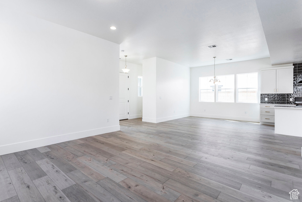 Unfurnished living room featuring an inviting chandelier and light wood-type flooring