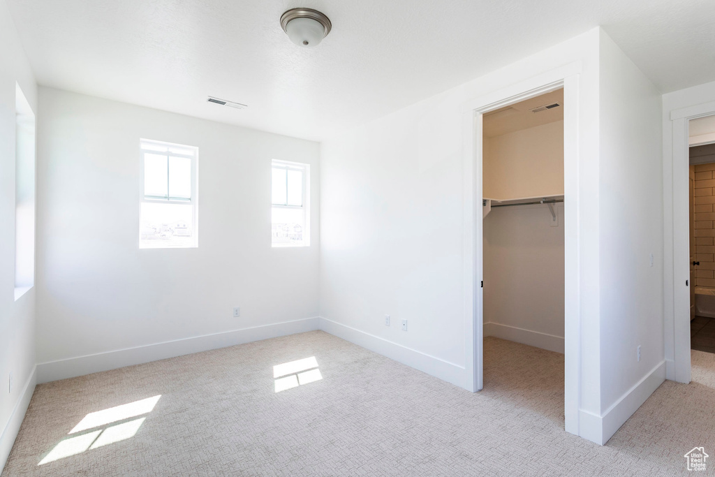 Unfurnished bedroom with light carpet, a closet, and a walk in closet