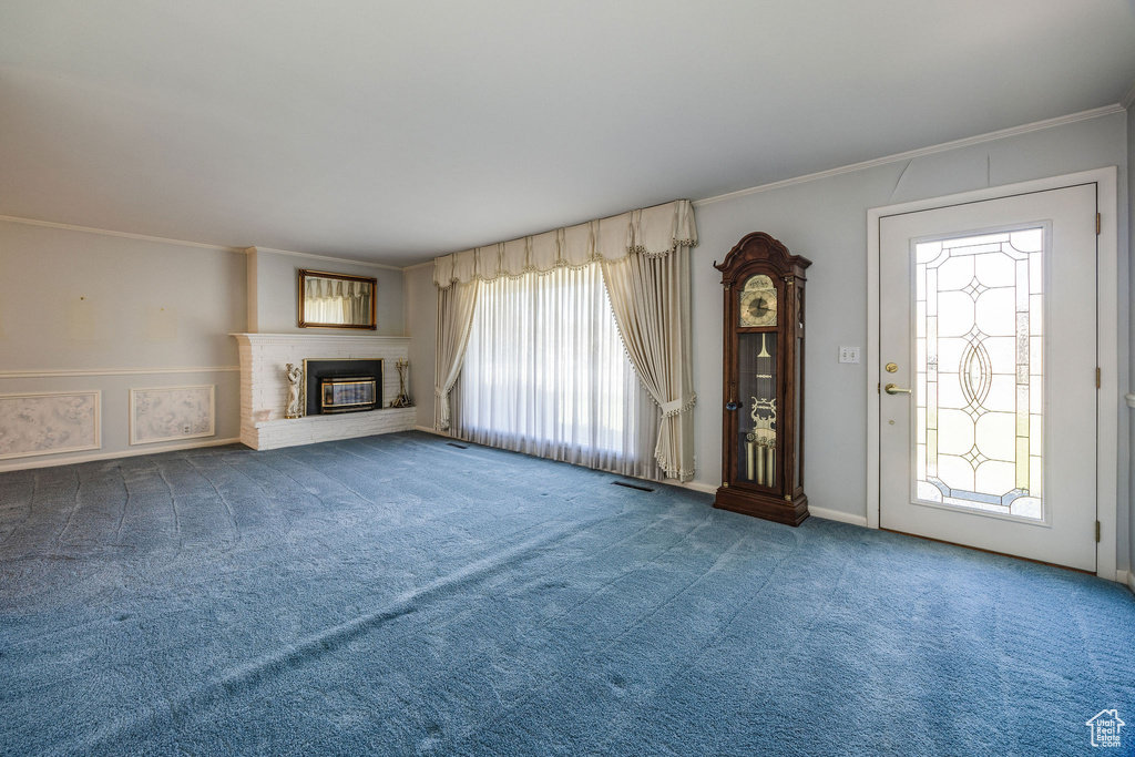 Unfurnished living room featuring carpet floors, a healthy amount of sunlight, a fireplace, and crown molding