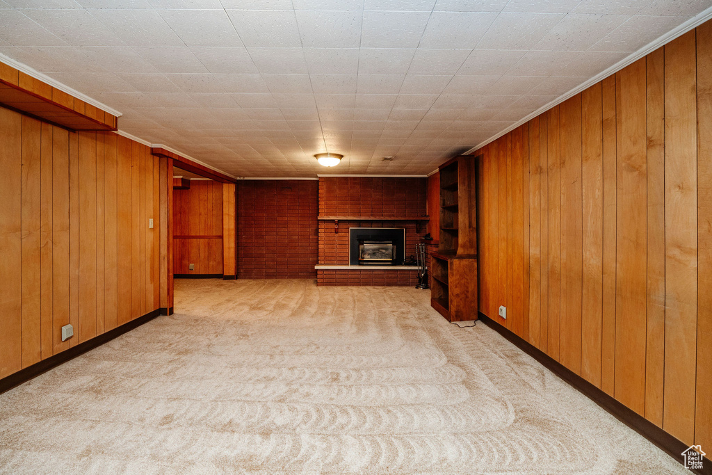 Unfurnished living room featuring crown molding, wood walls, light colored carpet, and a brick fireplace