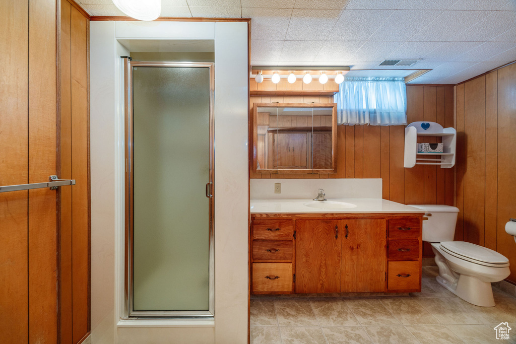 Bathroom featuring wood walls, a shower with door, toilet, and vanity