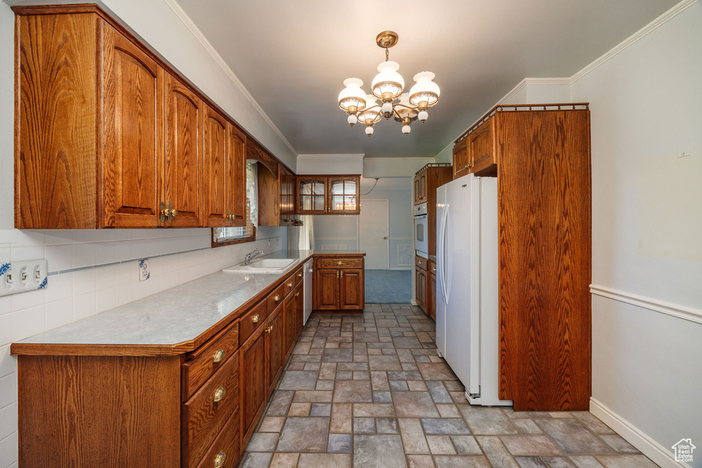 Kitchen featuring backsplash, white appliances, pendant lighting, crown molding, and a chandelier