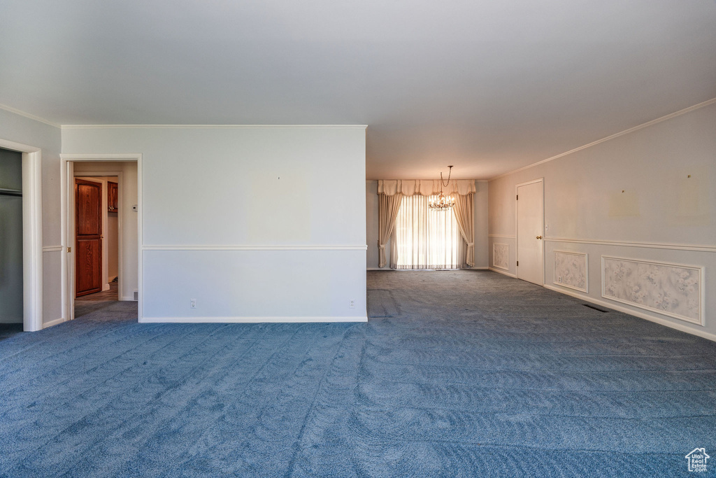 Carpeted spare room featuring crown molding and a notable chandelier