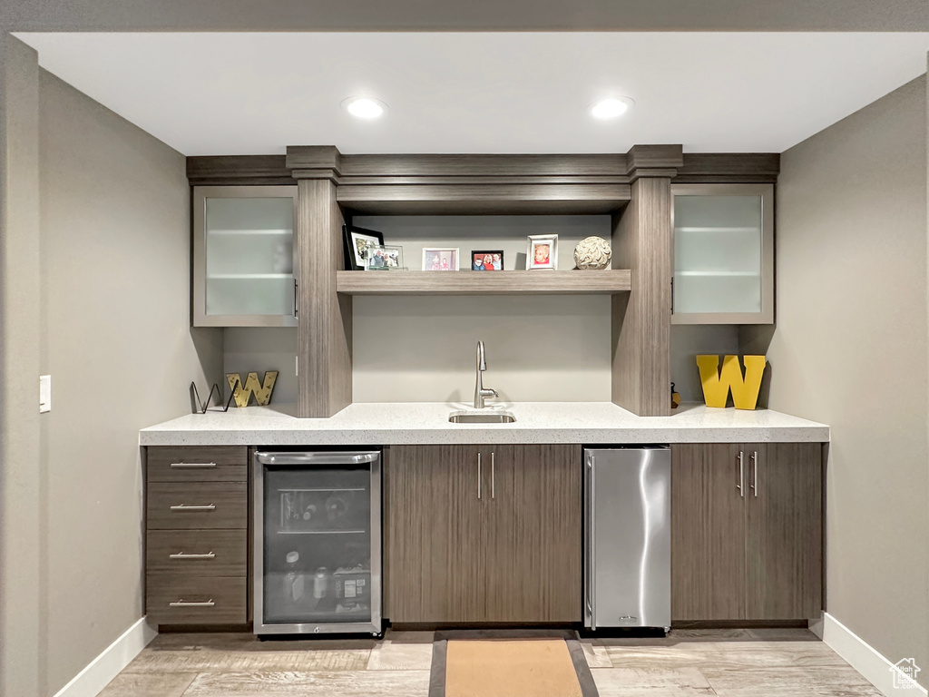 Bar with dark brown cabinets, beverage cooler, stainless steel fridge, and sink