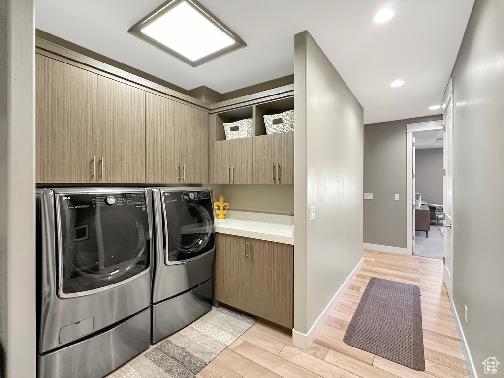 Clothes washing area featuring cabinets, light hardwood / wood-style floors, and washer and dryer