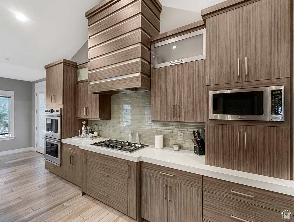 Kitchen with appliances with stainless steel finishes, backsplash, lofted ceiling, and light hardwood / wood-style flooring