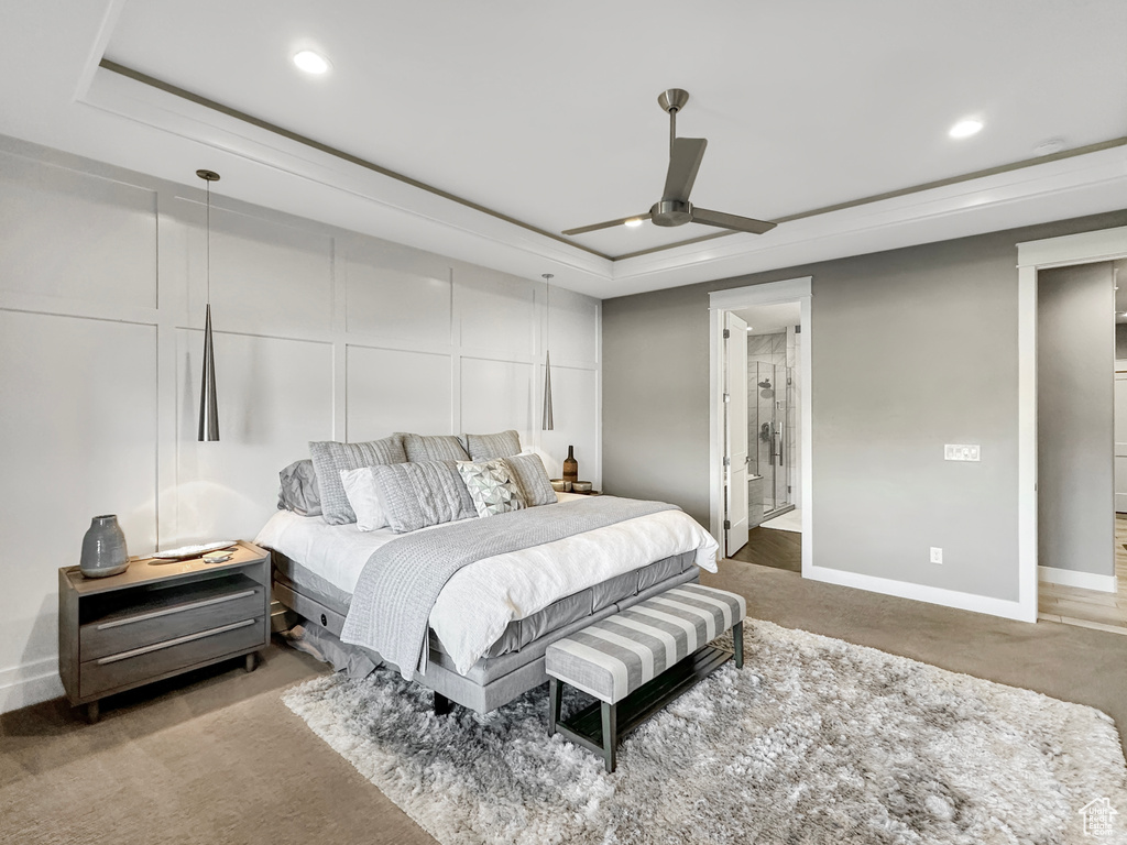 Carpeted bedroom featuring a tray ceiling, ensuite bath, and ceiling fan