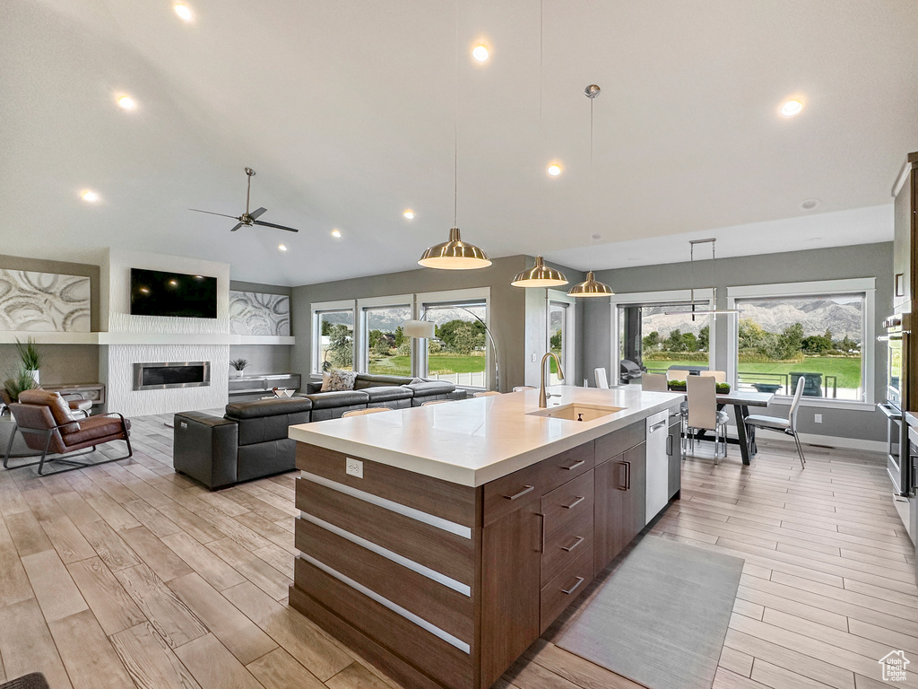 Kitchen featuring ceiling fan, an island with sink, sink, decorative light fixtures, and light hardwood / wood-style flooring