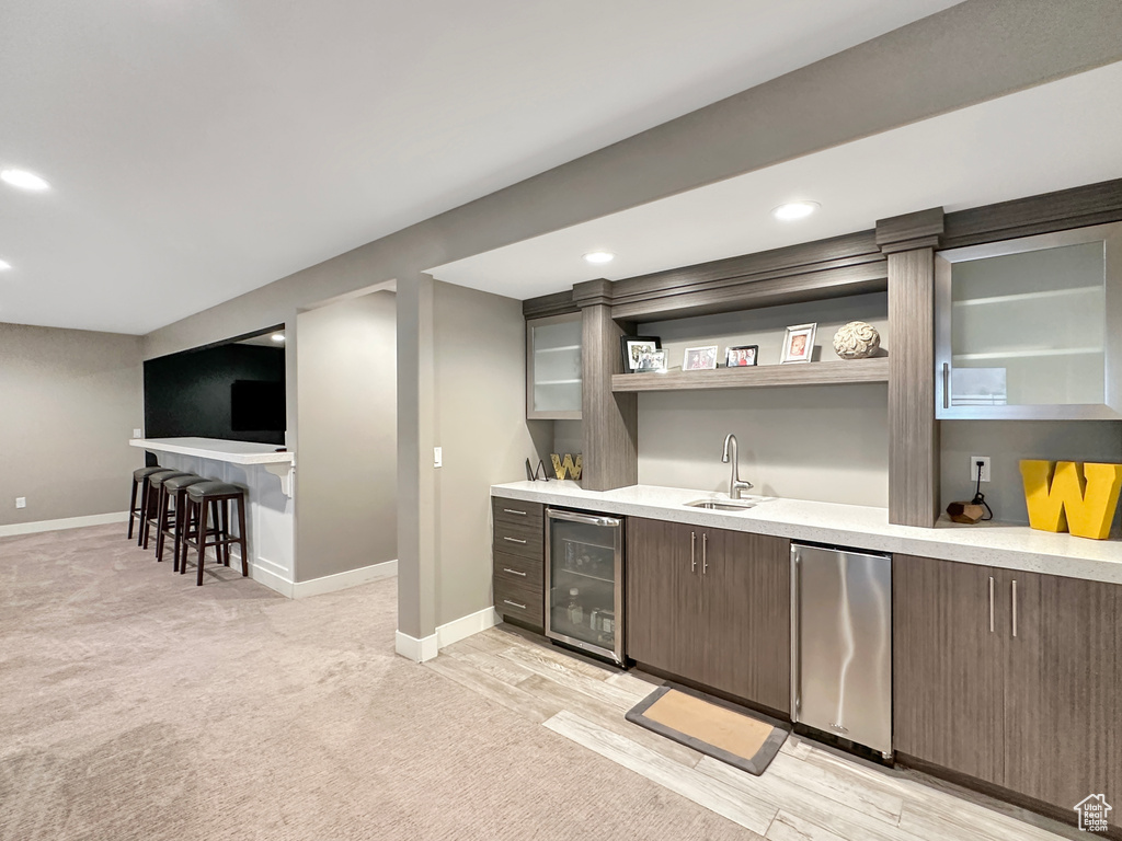 Bar with sink, dark brown cabinets, beverage cooler, stainless steel refrigerator, and light carpet