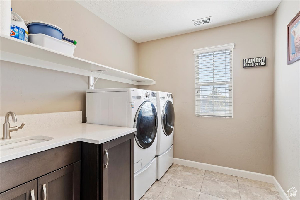 Laundry area featuring light tile patterned flooring, sink, a textured ceiling, cabinets, and separate washer and dryer