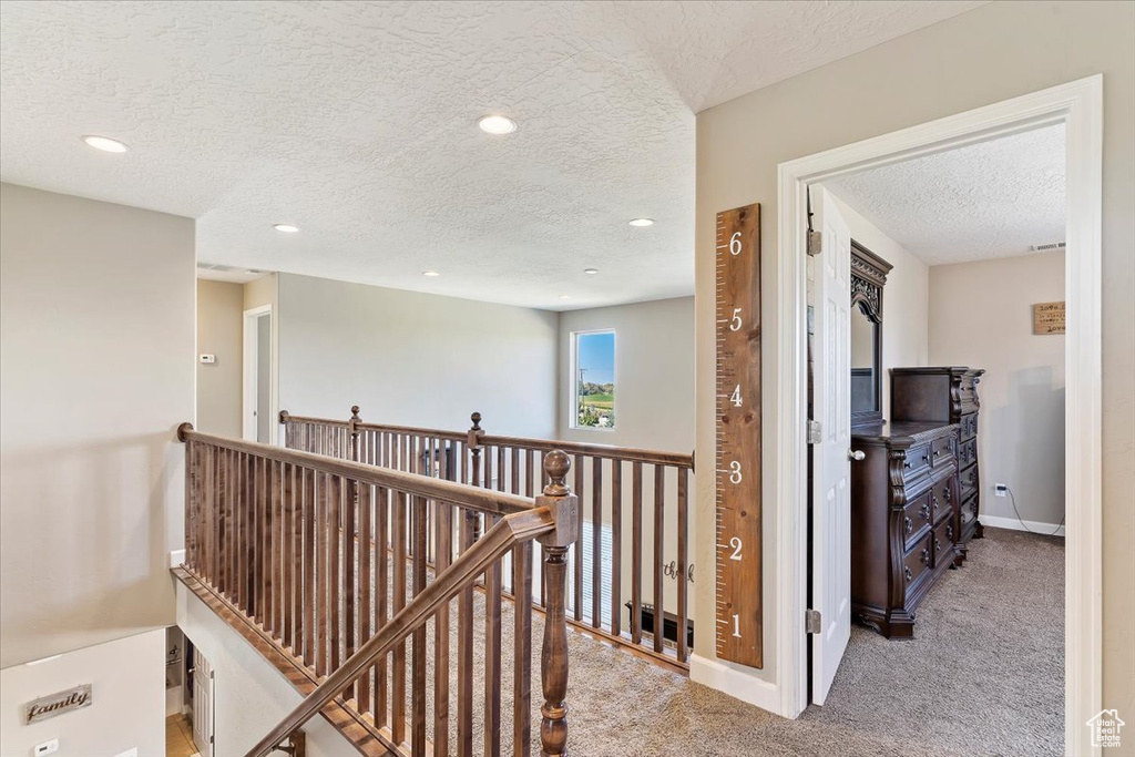 Corridor featuring a textured ceiling and light carpet