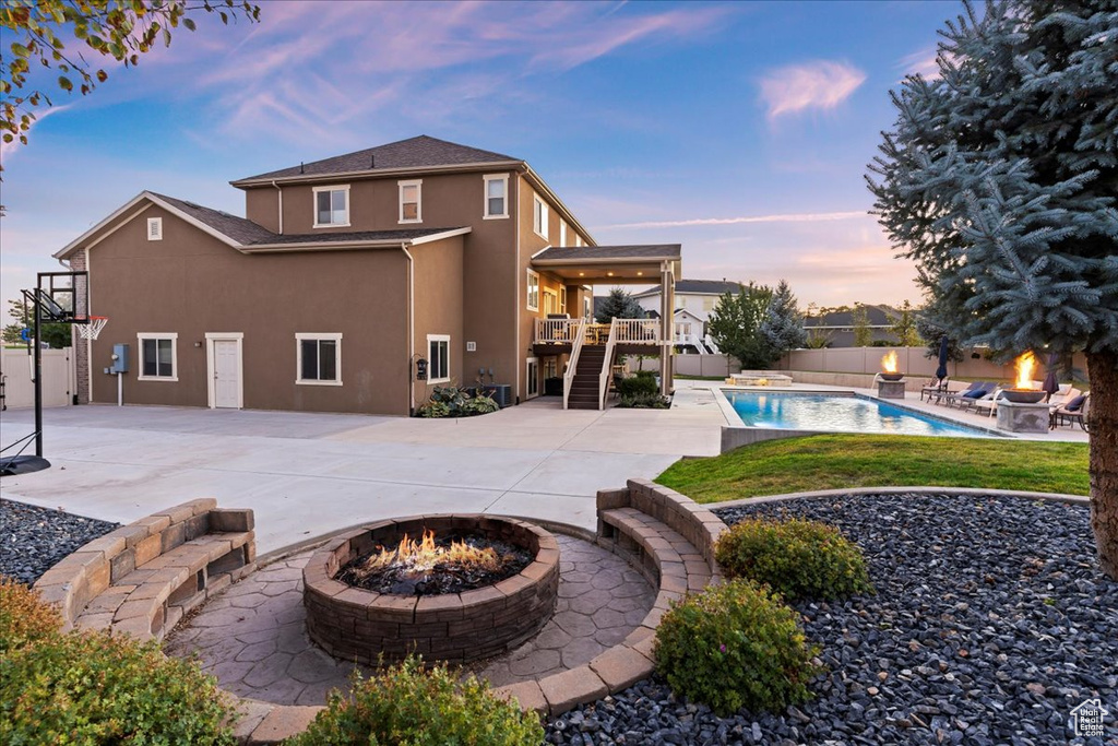 Back house at dusk featuring a fire pit, a fenced in pool, and a patio