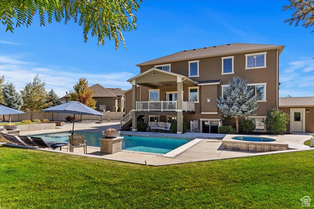 Back of property featuring a lawn, a balcony, a patio area, and a pool with hot tub