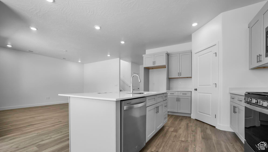 Kitchen featuring light hardwood / wood-style floors, range, sink, a center island with sink, and stainless steel dishwasher