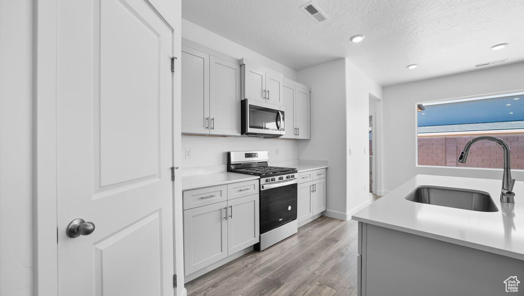 Kitchen with light hardwood / wood-style floors, a textured ceiling, sink, white cabinetry, and stainless steel appliances