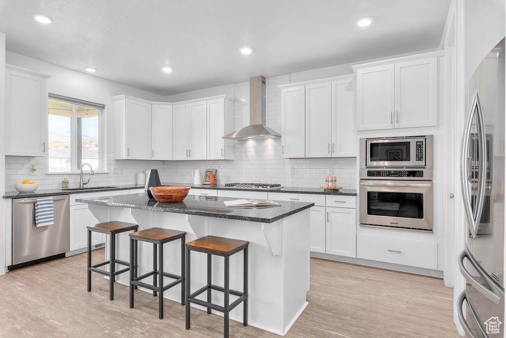 Kitchen featuring a center island, wall chimney range hood, stainless steel appliances, and white cabinets