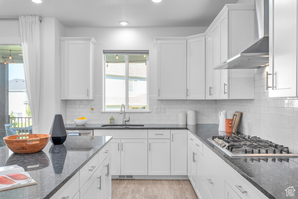 Kitchen with white cabinets, wall chimney range hood, and decorative backsplash