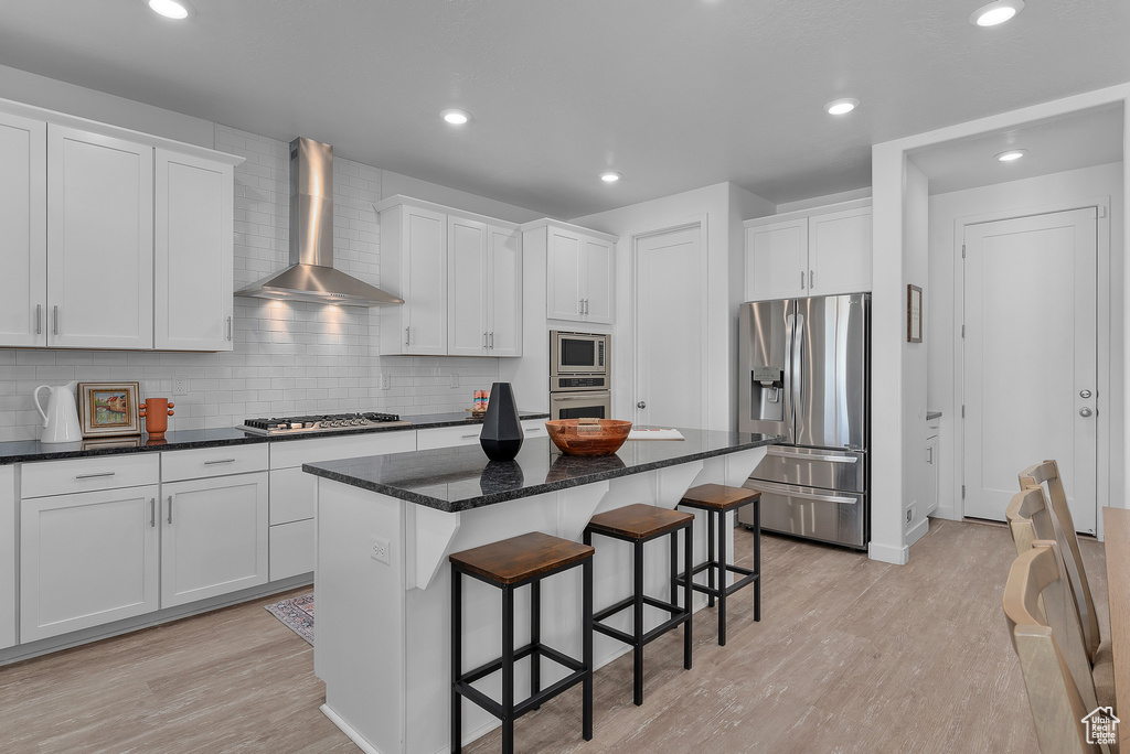 Kitchen with light hardwood / wood-style flooring, stainless steel appliances, wall chimney range hood, and white cabinetry