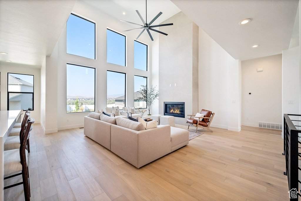 Living room featuring ceiling fan, a fireplace, a towering ceiling, and light hardwood / wood-style floors