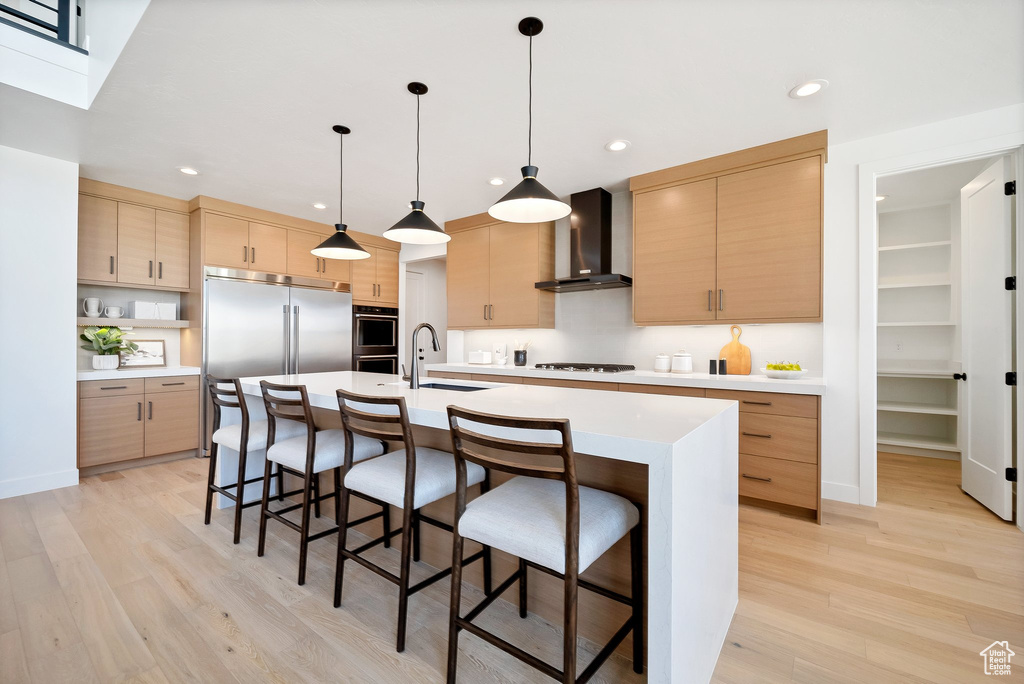 Kitchen featuring hanging light fixtures, wall chimney exhaust hood, light brown cabinetry, and light hardwood / wood-style flooring