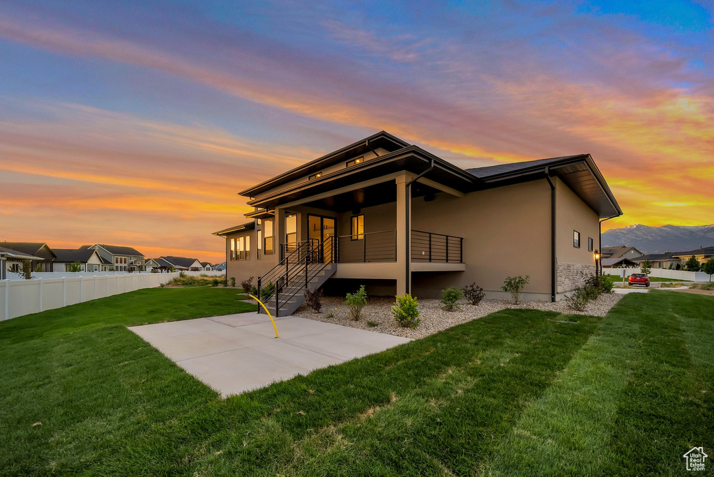 Back house at dusk featuring a yard and a patio