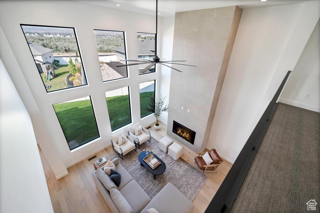 Unfurnished living room with ceiling fan, hardwood / wood-style flooring, a tiled fireplace, and a high ceiling