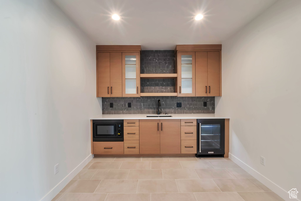 Bar with light brown cabinets, wine cooler, sink, black microwave, and decorative backsplash