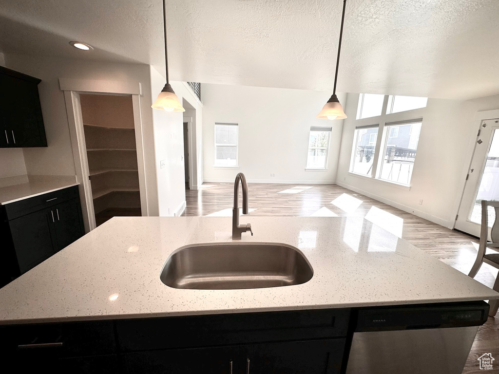 Kitchen featuring pendant lighting, light wood-type flooring, sink, an island with sink, and light stone countertops