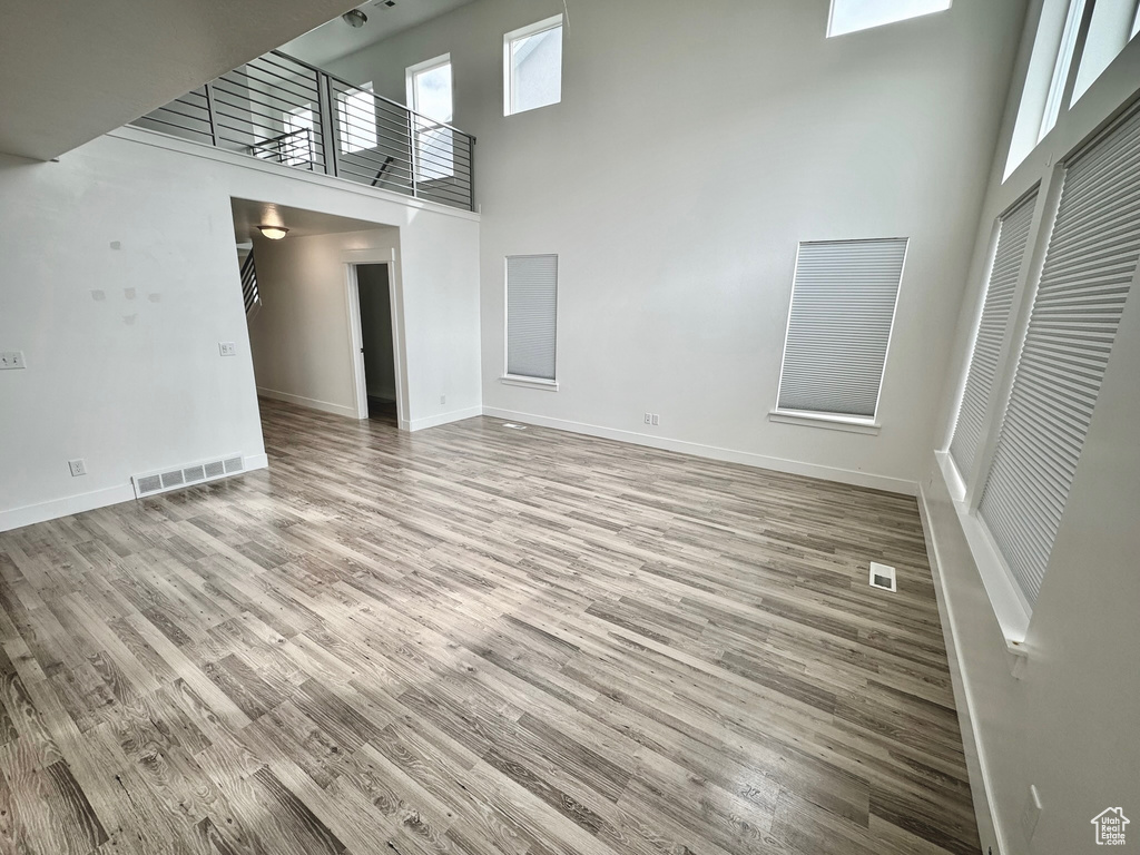 Unfurnished living room with light wood-type flooring and a towering ceiling