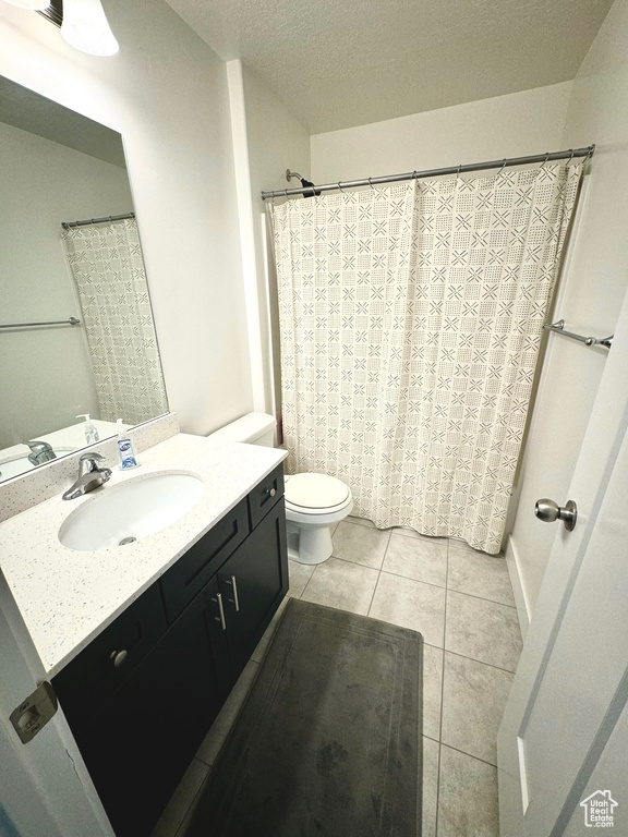 Bathroom featuring a textured ceiling, toilet, tile patterned floors, vanity, and curtained shower