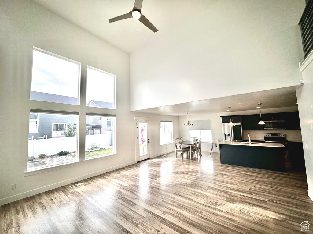 Unfurnished living room with ceiling fan, sink, hardwood / wood-style floors, and high vaulted ceiling